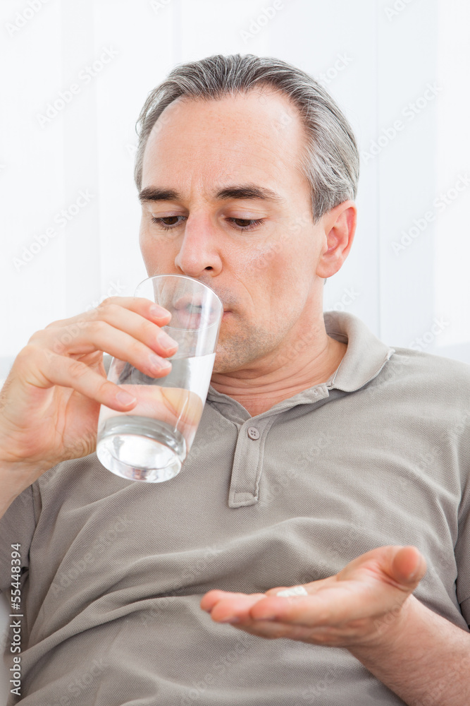 Ill man taking medication sitting up holding a glass of water Ill man taking medication sitting up holding a glass of water
