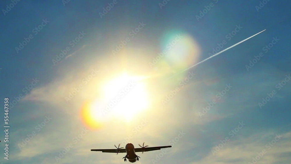 Airplane landing silhouette through sun rays, daytime, blue sky Airplane landing silhouette through sun rays, daytime, blue sky