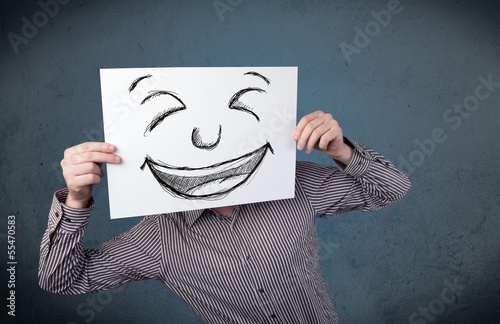 Businessman holding a paper with smiley face in front of his hea photo