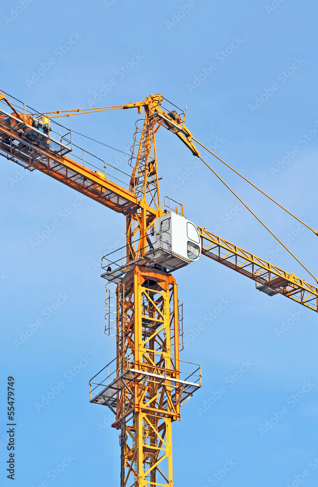 Yellow construction tower crane against blue sky Yellow construction tower crane against blue sky