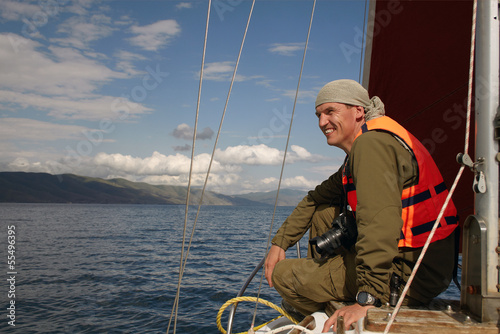 The smiling man in a life jacket sits on a nose of the yacht flo