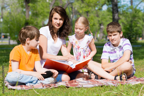 teacher reads a book to children in a summer park © adam121