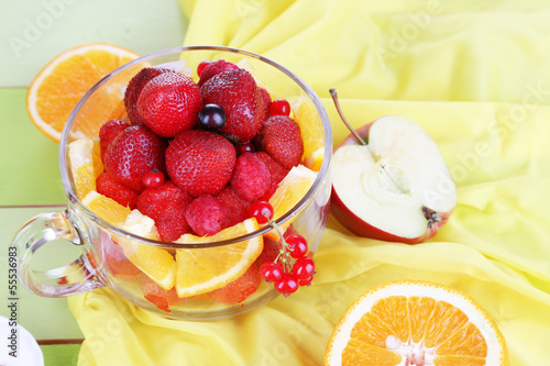 Useful fruit salad in glass cup on wooden table close-up