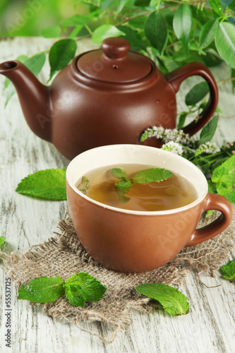 Teapot and cup of herbal tea with fresh mint flowers