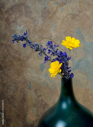 Blue and yelow wildflowers in a turquoise vase against a rustic photo