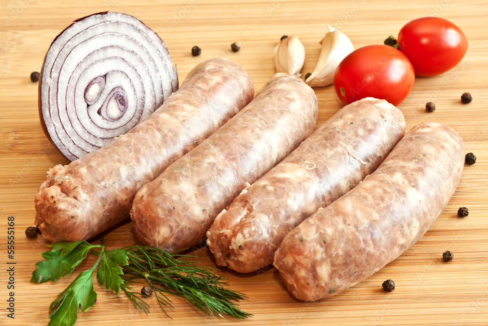Uncooked sausages with vegetables on the chopping board Uncooked sausages with vegetables on the chopping board