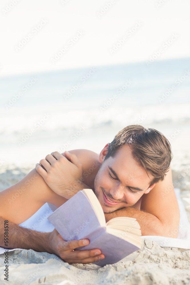 Smiling handsome man on the beach reading