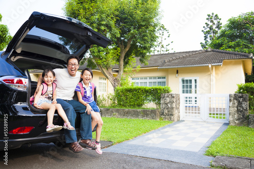 happy family sitting in the car and their house behind