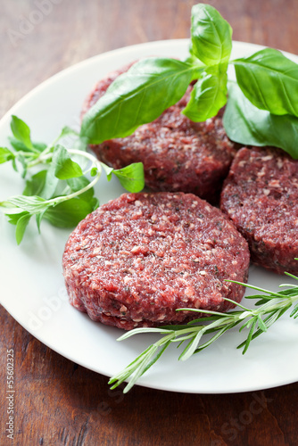 Raw beef hamburger patties with fresh herbs before cooking .