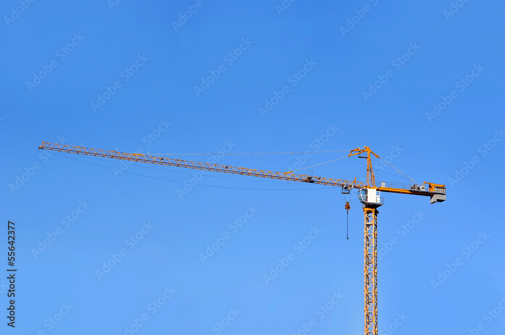 Yellow construction tower crane against blue sky Yellow construction tower crane against blue sky