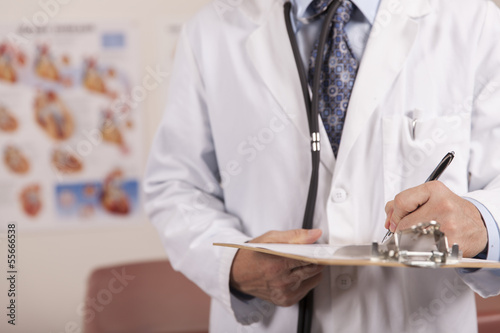 A male doctor writes on a patients chart.