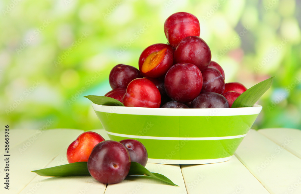 Ripe plums in bowl on wooden table on natural background Ripe plums in bowl on wooden table on natural background