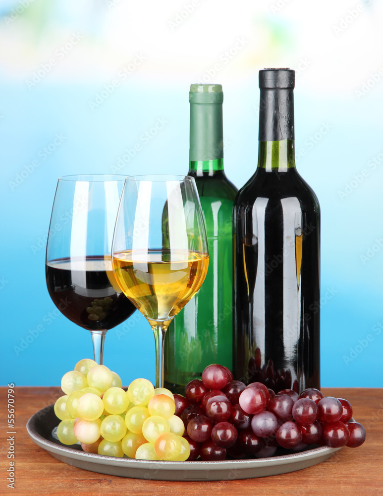 Wine bottles and glasses of wine on tray, on bright background