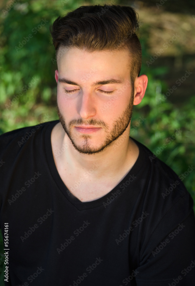 Fototapeta premium Peaceful young man with eyes closed, relaxing outdoors in nature
