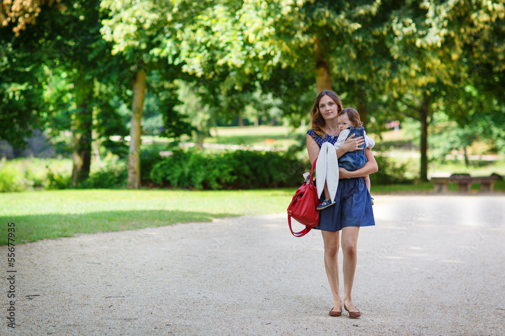 Beautiful mother and little daughter walking in summer park