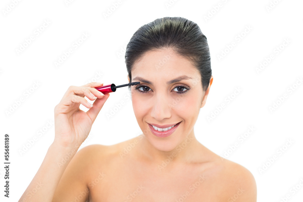 Brunette applying mascara and smiling at camera Brunette applying mascara and smiling at camera