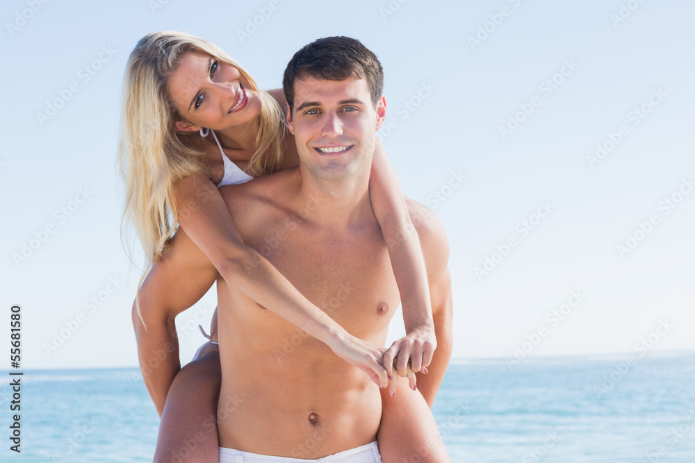 Happy man giving his pretty girlfriend a piggy back smiling at c