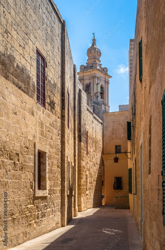 Tiny street in Mdina with limestone buildings and a church