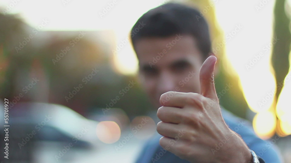 Young man outdoors thumb up rack focus in park daytime Young man outdoors thumb up rack focus in park daytime