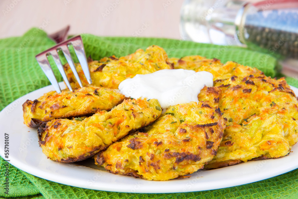 Zucchini pancakes with carrots and sour cream on green towel Zucchini pancakes with carrots and sour cream on green towel