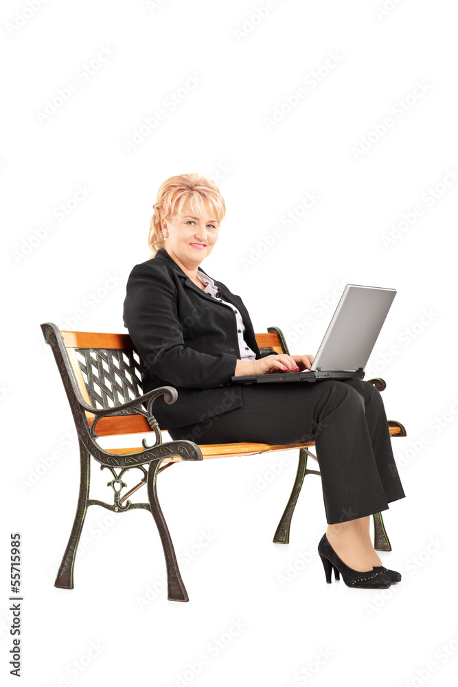 Mature businesswoman sitting on bench and working on laptop Mature businesswoman sitting on bench and working on laptop