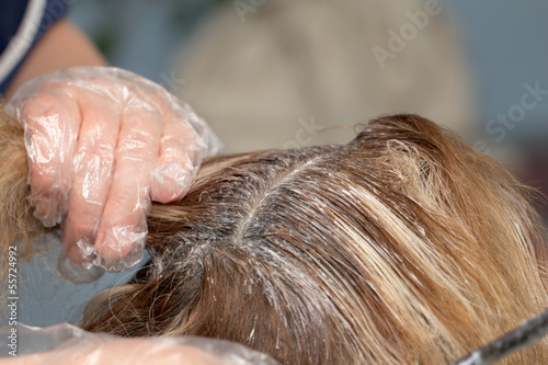 beautician applying hair dye on female customer's hair