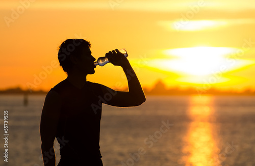 Man drinking bottle of water on the beach at sunrise