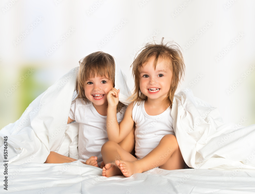 happy little girl's twin sister in bed under the blanket having