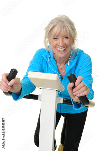 Sportliche Seniorin auf dem Hometrainer hört Musik photo