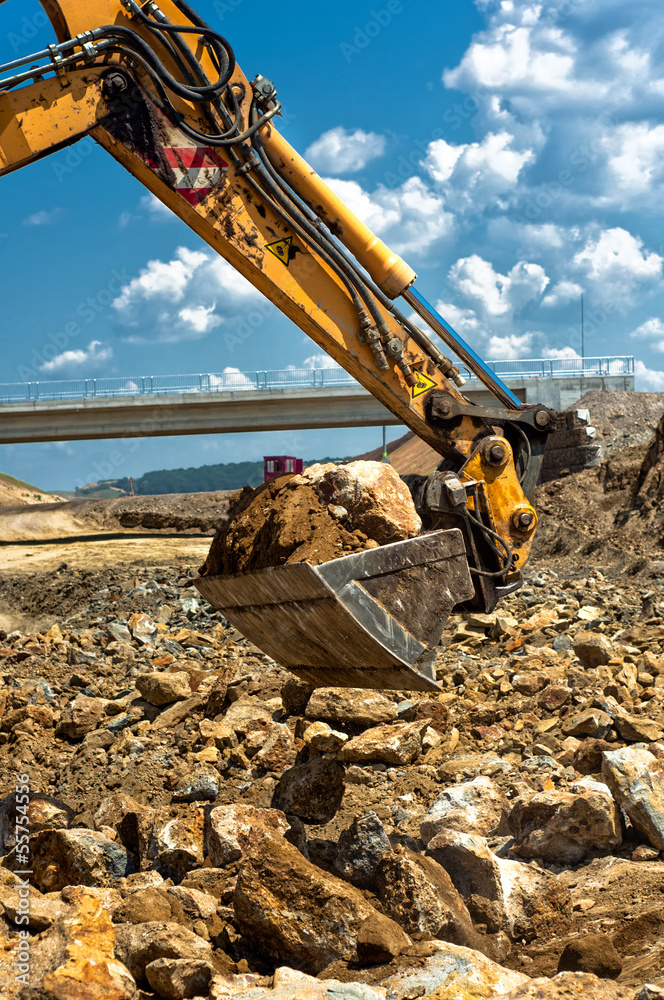 Fototapeta premium professional worker moving excavator scoop while loading dumper