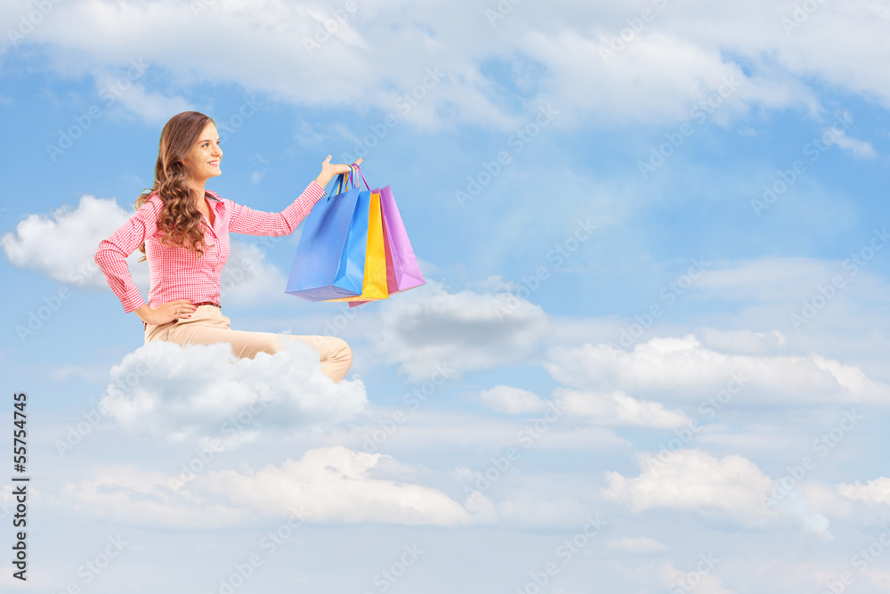 Young female flying on cloud and holding bags against cloudy sky