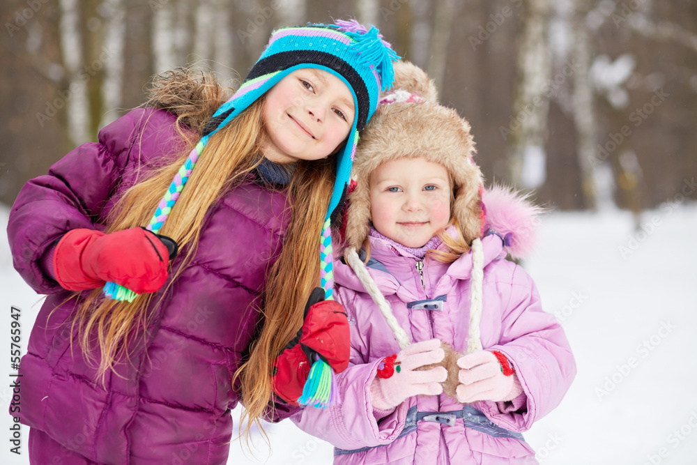 Two smiling girls stand side by side in winter park Two smiling girls stand side by side in winter park