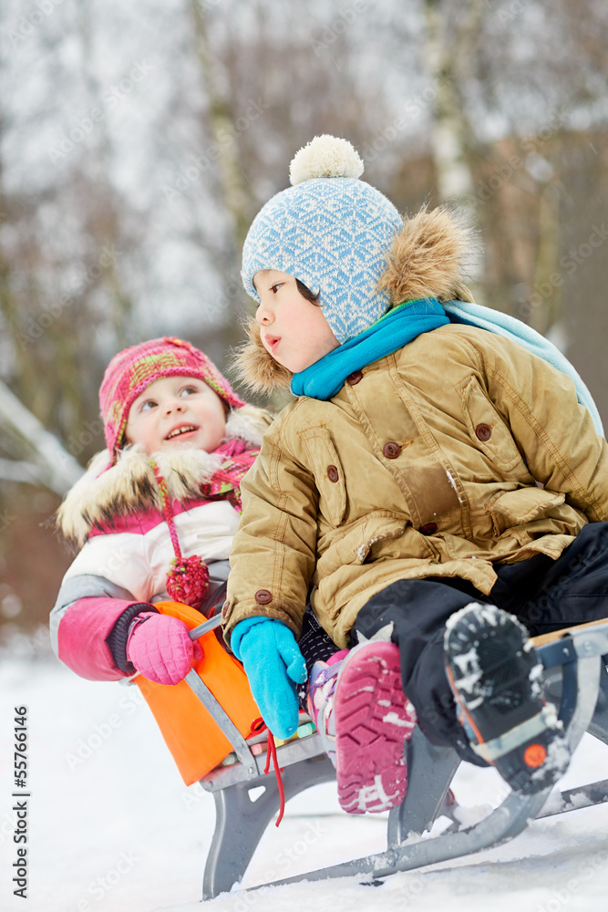 Little children sit in sled in winter park, focus on first child