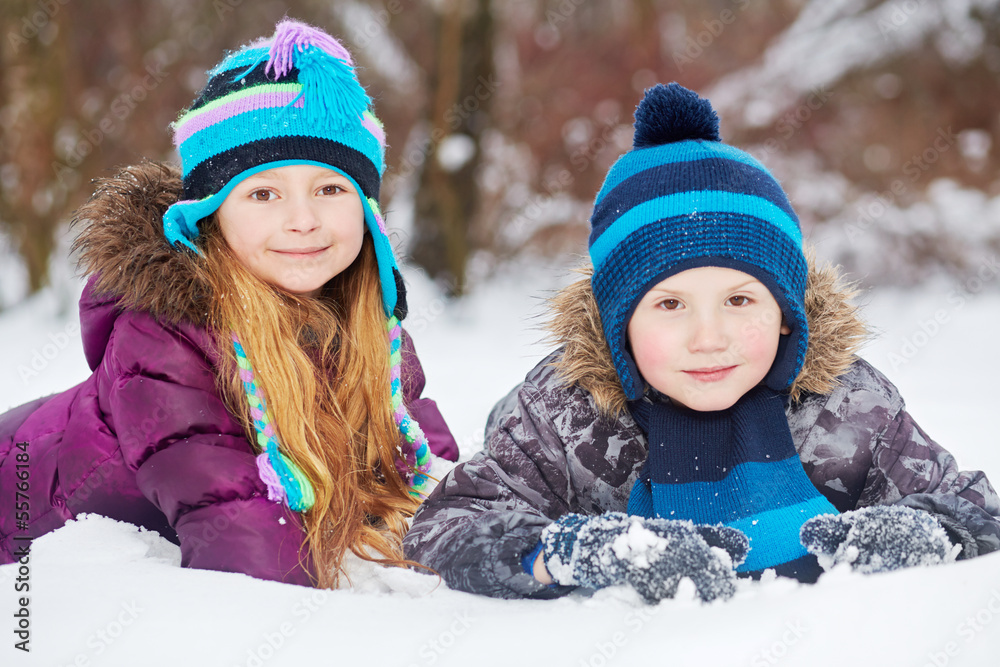 Smiling little girl and boy lie side by side on snowdrift