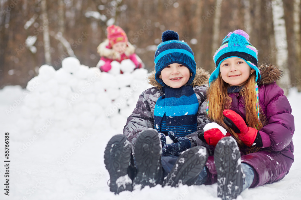 Smiling boy and girl sit nearby on snow and little girl