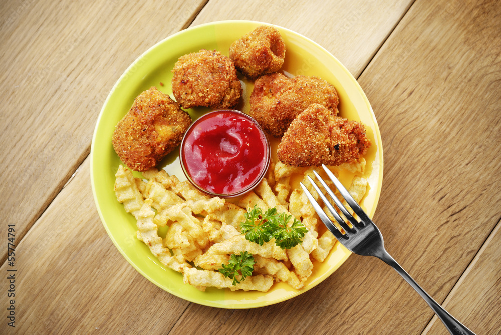 French fries and chicken on the plate on the wooden table French fries and chicken on the plate on the wooden table