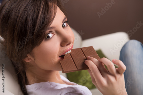 Woman eating chocolate. Beautiful young woman sitting on the coa