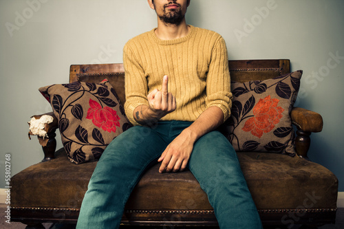 Vászonkép Young man on sofa displaying obscene gesture