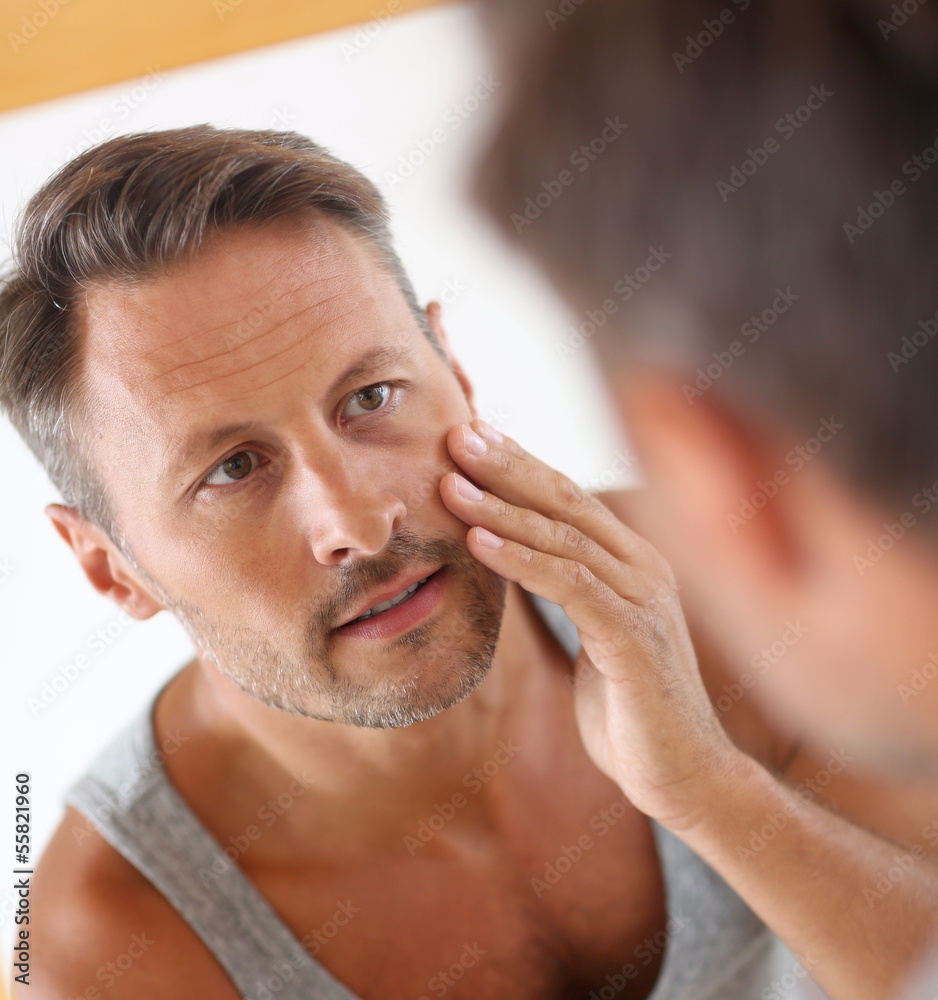 Obraz premium Man in bathroom applying cosmetics on his face