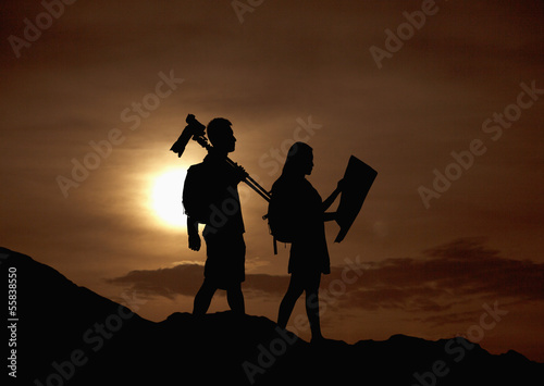 Silhouette of two people hiking and carrying camera and a map in nature at sunset