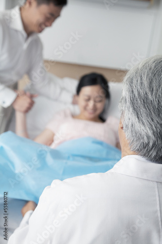 Women in labor holding her husbands hand with doctor in the foreground in the hospital