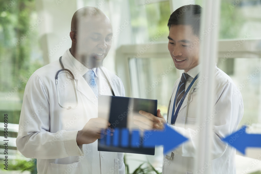 Two doctors consulting over medical record on the other side of glass doors