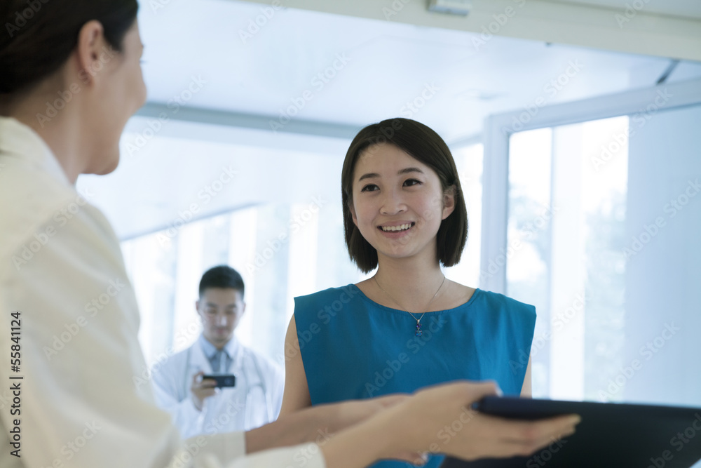 Smiling doctor and patient standing by the counter in the hospital looking down at medical record Smiling doctor and patient standing by the counter in the hospital looking down at medical record