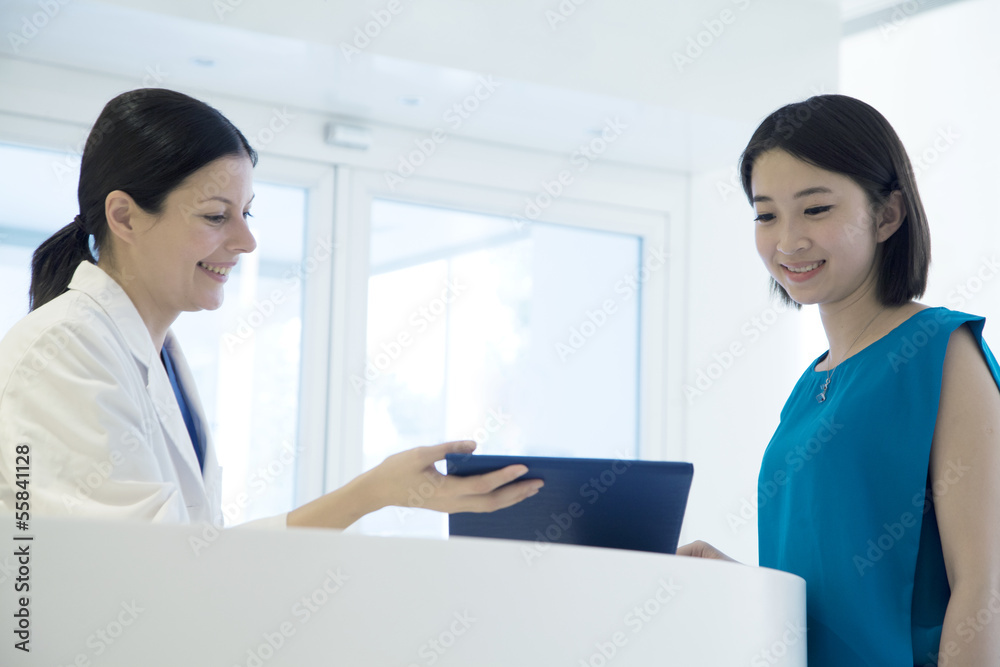Smiling doctor and patient standing by the counter in the hospital looking down at medical record Smiling doctor and patient standing by the counter in the hospital looking down at medical record