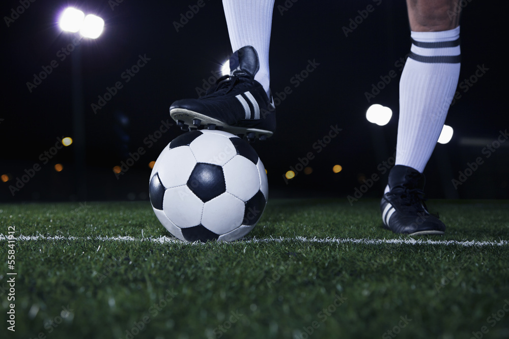 Close up of feet on top of soccer ball on the line, night time in the stadium