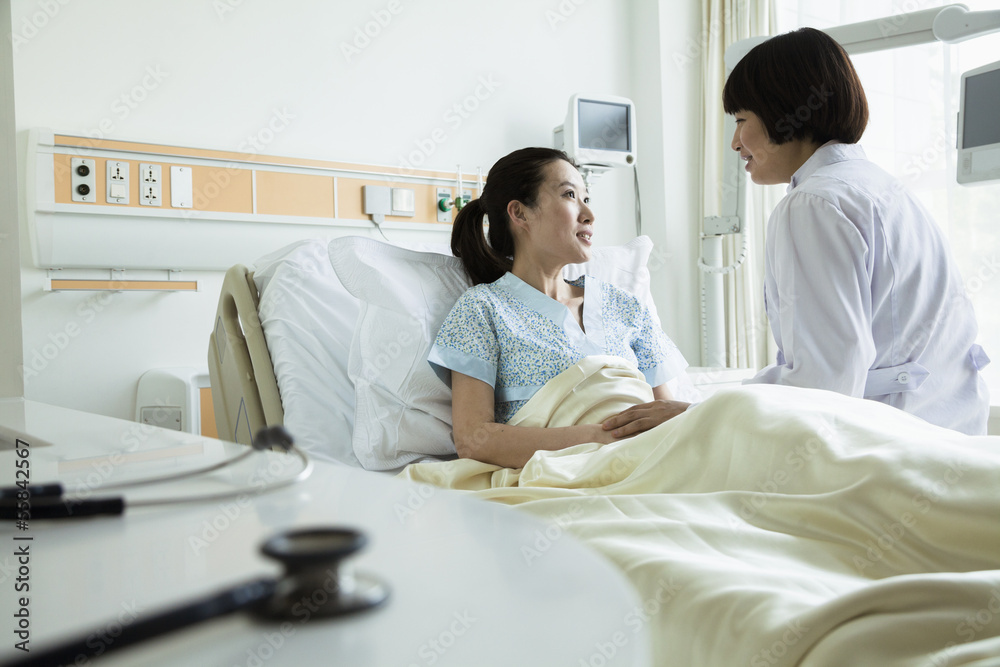 Female doctor sitting on hospital bed and discussing with young female patient Female doctor sitting on hospital bed and discussing with young female patient