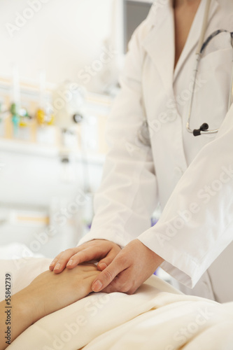 Close up of doctor holding a patients hands lying down on a hospital bed