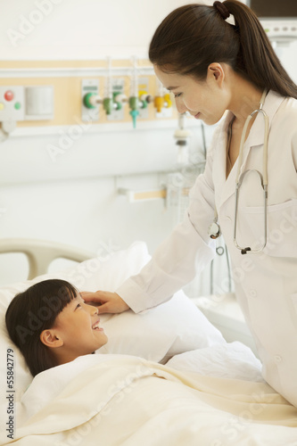 Female doctor talking to girl patient lying down on a hospital bed
