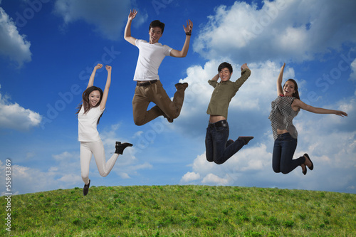 Four smiling friends jumping in mid-air  sky and cloud background