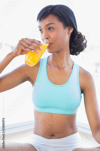 Pensive fit woman drinking a glass of orange juice